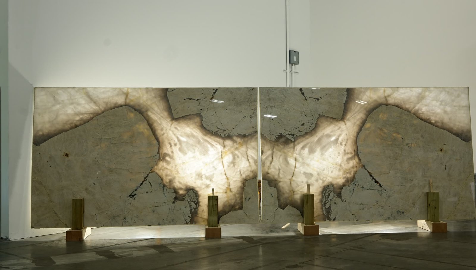 A mirrored pair of stone panels standing side by side, lit from behind so the pattern glows through, with the two halves forming a symmetrical figure across the join.