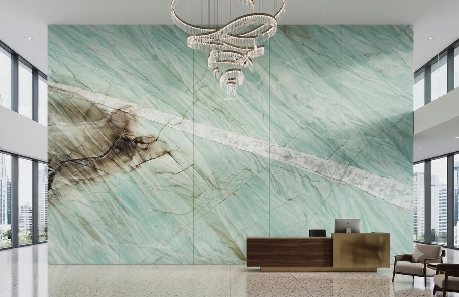 Rendered visualisation of a double-height lobby with a full-wall panelled installation of pale blue-green veined stone, a ring chandelier, floor-to-ceiling glazing on both sides and a low wood and brass reception desk.