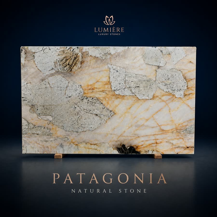 A polished stone slab with cream, grey and rust-orange veining, propped upright on small wooden blocks against a dark navy backdrop, captioned Patagonia Natural Stone beneath the Lumiere Luxury Stones wordmark.