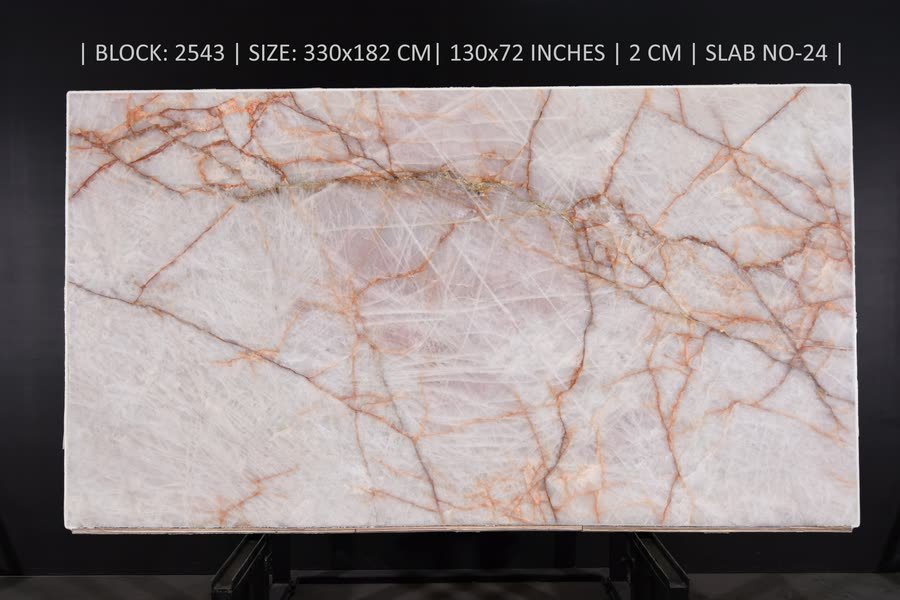 A full natural stone slab standing upright on a dark metal easel against a black studio wall, translucent creamy white with a soft blush centre and a network of thin rust-orange veins spreading across the surface. A line of printed specification text runs across the top of the image.