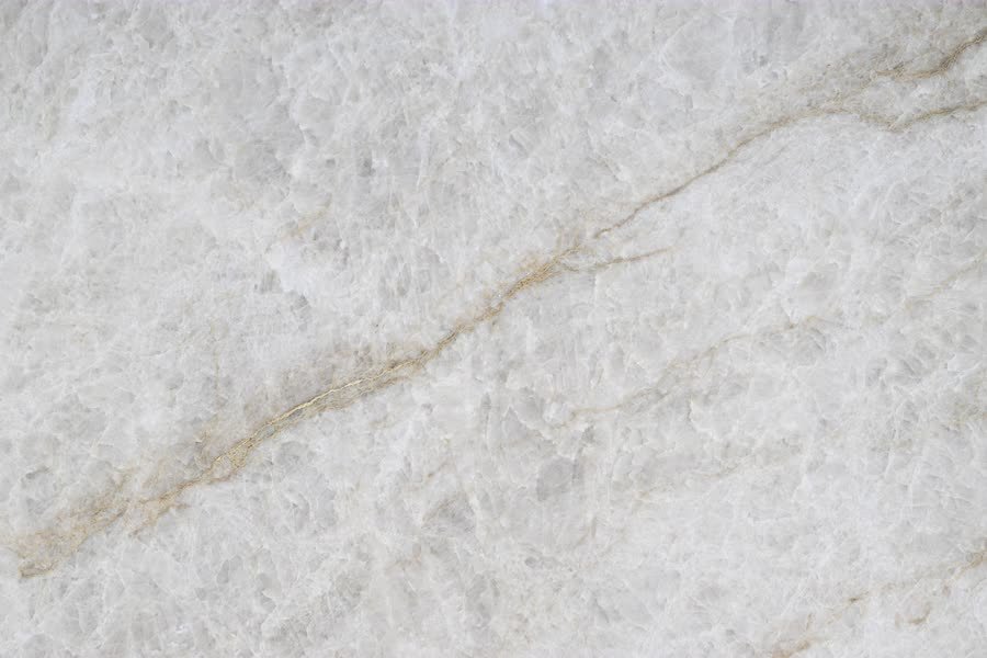 Extreme close-up of a translucent white crystalline stone surface, its icy facets shot through with a thin golden-brown vein running diagonally from lower left to upper right.
