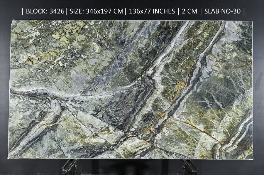 A full polished stone slab with dramatic green, grey and cream veining shot through with rust-orange and white seams, displayed upright on a stand against a dark backdrop. A line of white specification text runs across the top of the image.
