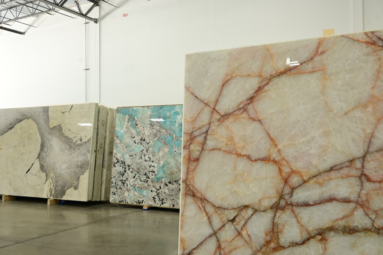 A pale crystalline slab with a branching orange-red vein network in the foreground, with further slabs receding behind it.