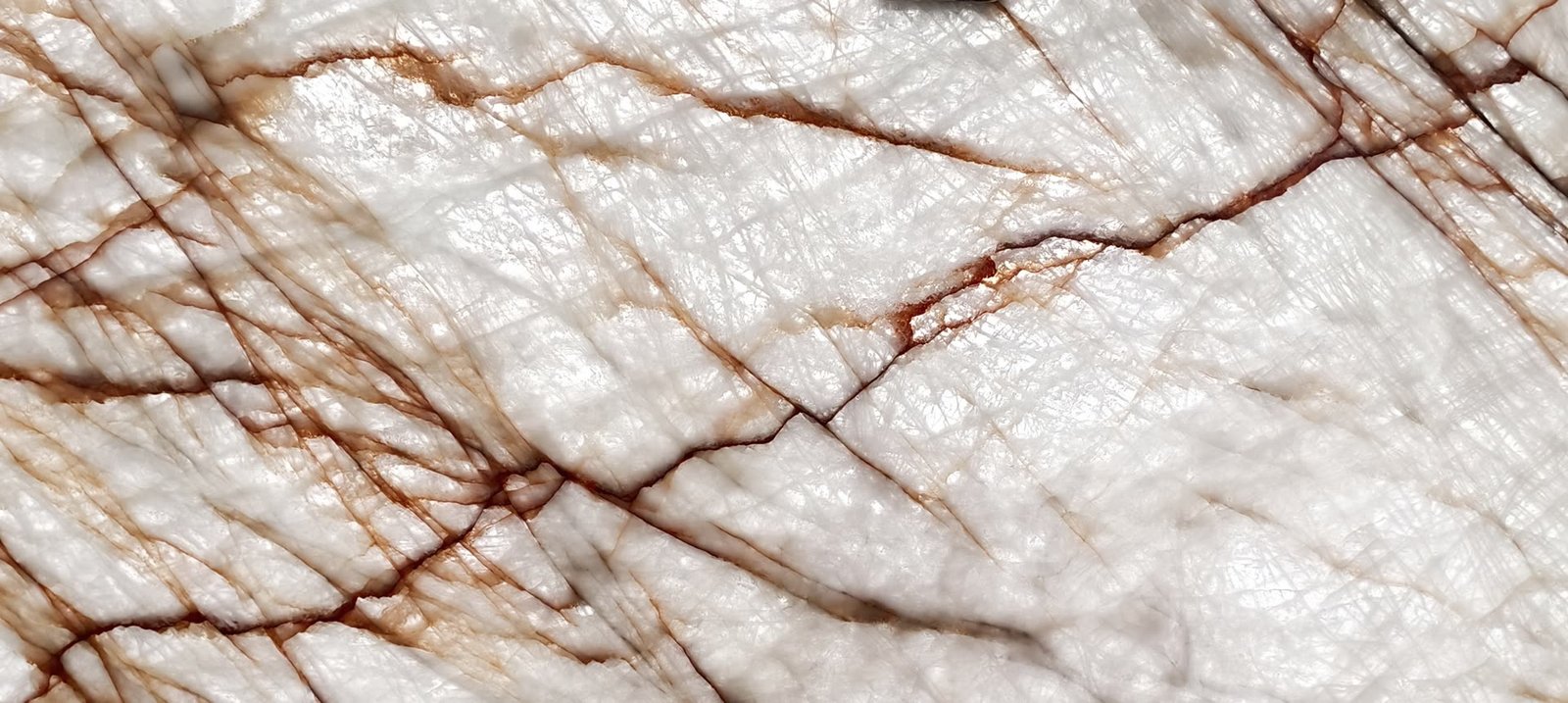 Backlit translucent stone with a dense network of rust-red veins glowing through a pale ground.